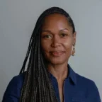 Headshot of Andrea Caupain Sanderson, CO-Founder and ED of Ile Komoyo, in a dark blue shirt in front of a gray background