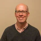 Headshot of Joel Bergsbaken over a tan background